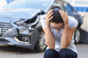 A woman at a broken car sits holding her head, close-up, blurry. Shock at the driver, after an accident on the road, emotional trauma