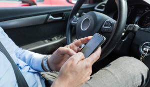 Businessman texting on his mobile phone while driving. Dangerous driver.